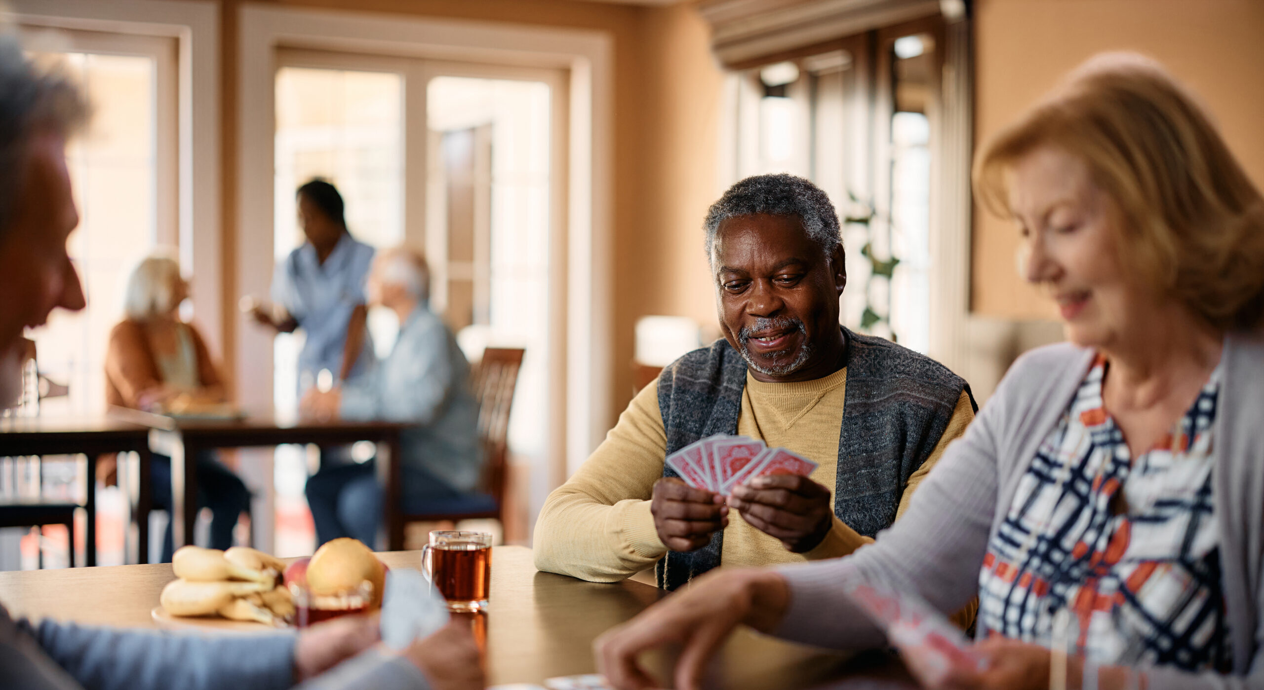 Happy black senior playing cards with friends in nursing home.