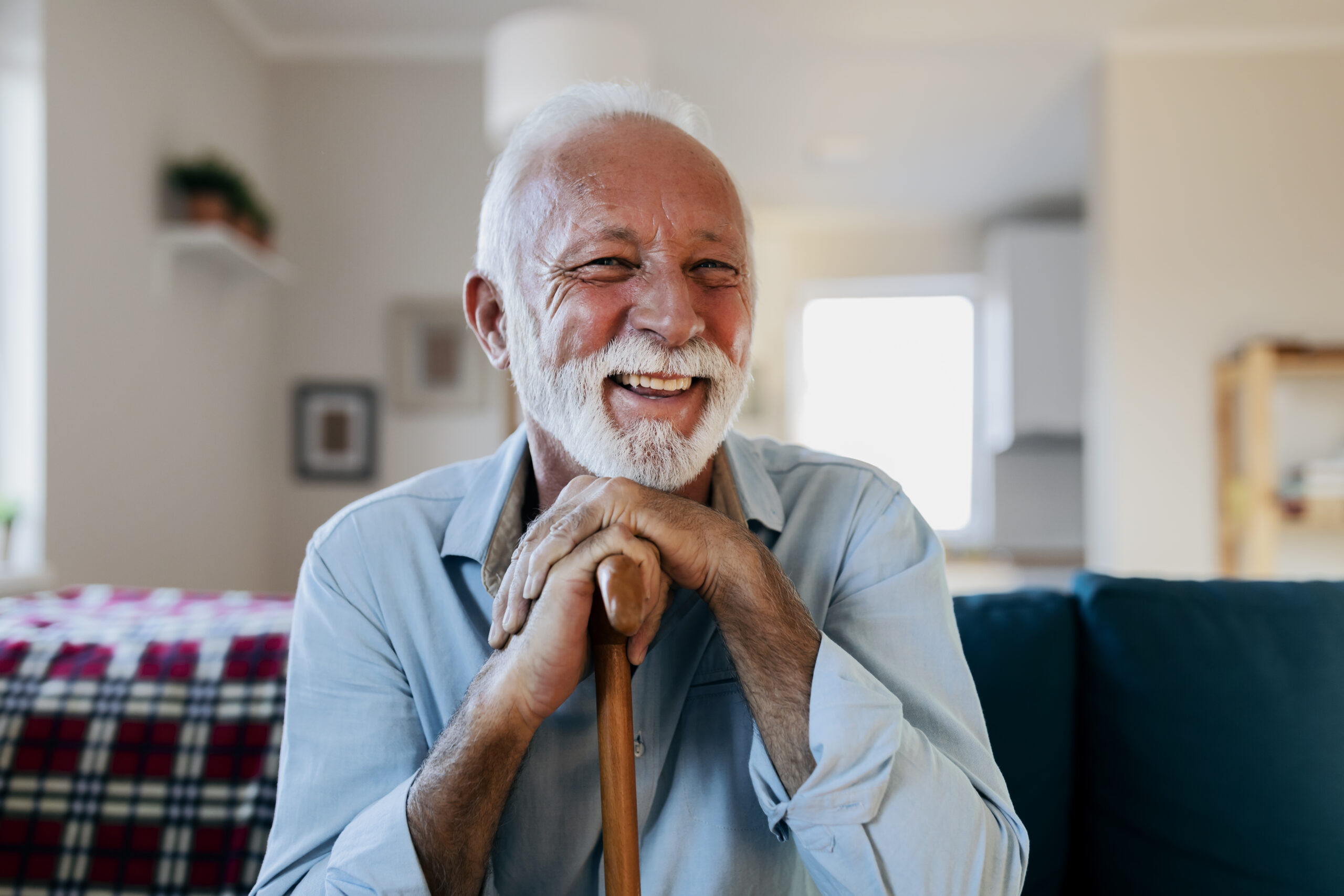 portrait of a happy senior man sitting and holding his walking stick in a nursing home during the morning