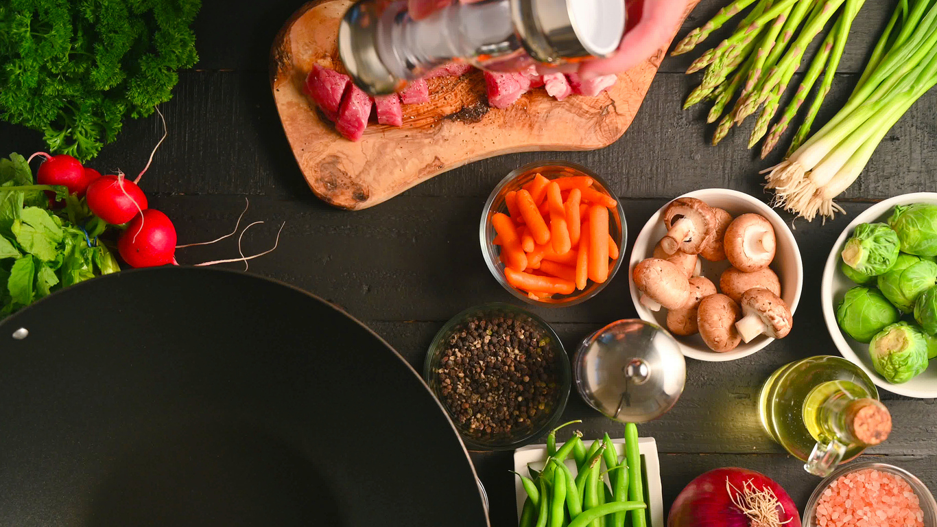 Chef salts fresh meat on a background of vegetables and a hot wok.Flat lay